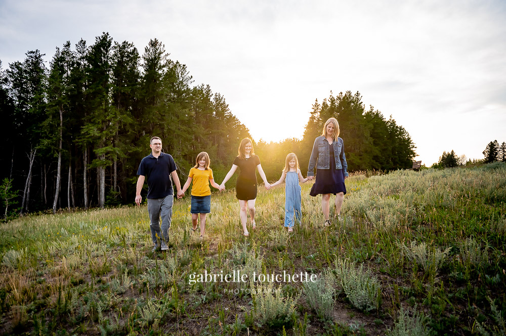 A family walking through Prairie grass in front of an evergreen forest at birds Hill Park in Manitoba