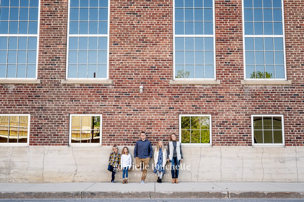A family posing in front of a large brick building with tall windows at the forks in Winnipeg