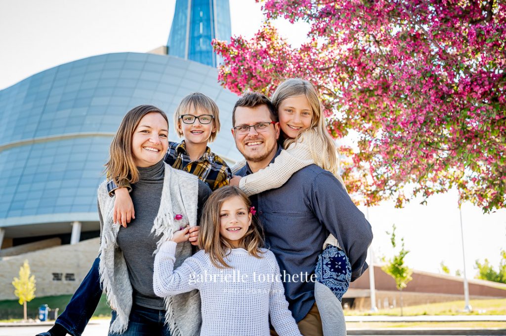 A family photo session standing in front of the human rights museum and a Cherry tree in full Blossom in the spring time in Winnipeg