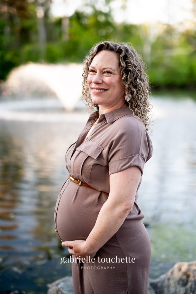 A maternity portrait photo taken in front of the Saint-Vital Park duck pond with a water fountain in the back