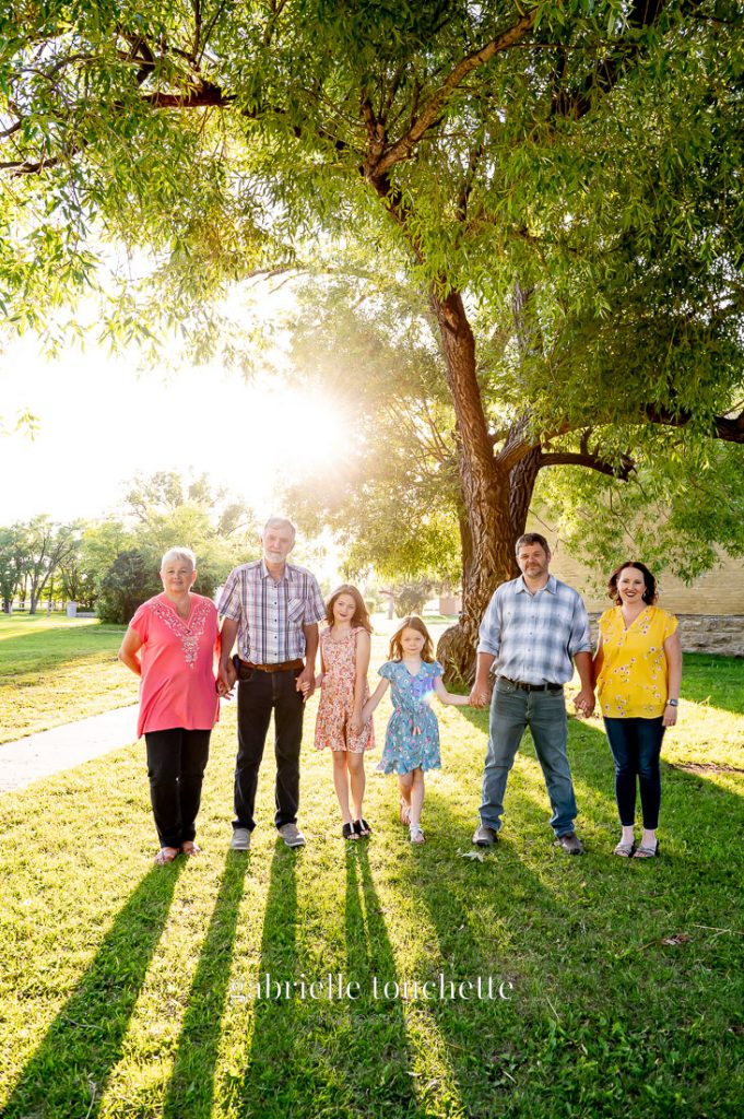 A multi family photo taken in front of a large tree at sunset with Long shadows from the hazy sunlight