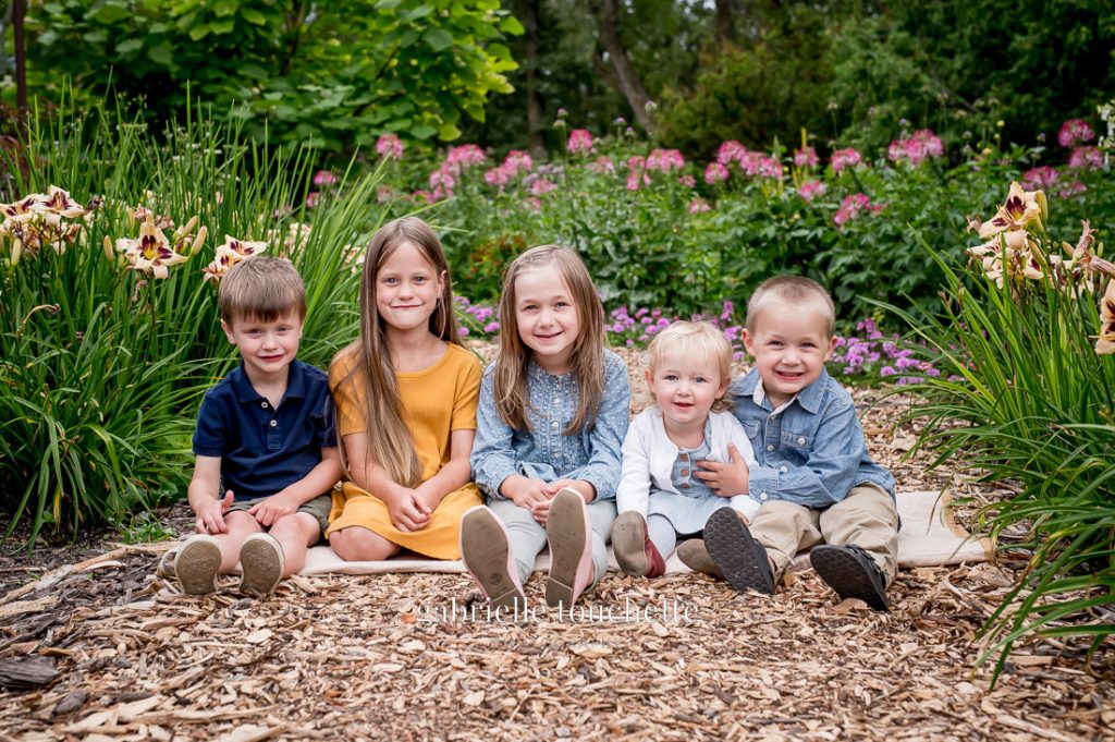A multi family photo session with cousins sitting on the ground at the English garden at Assiniboine park in Winnipeg