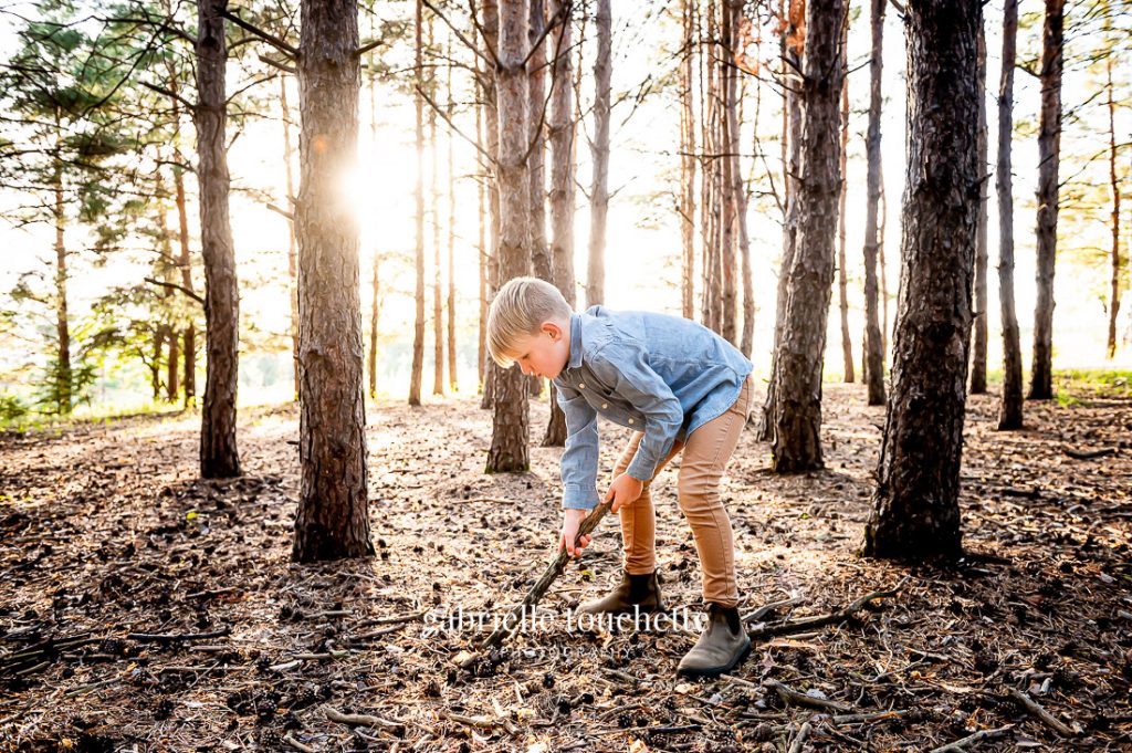 A boy plays with a stick inside an evergreen forest at sunset