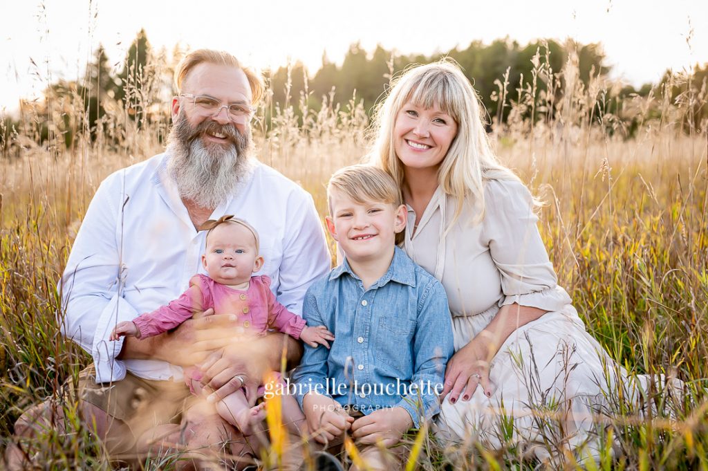 A casual family photo sitting in tall grass in the fall at a park in Manitoba during a sunset photo shoot
