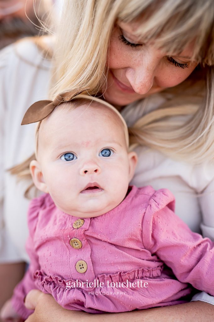A baby with blue eyes looking up towards the sky while her mother tenderly hugs her for a close-up photo capture