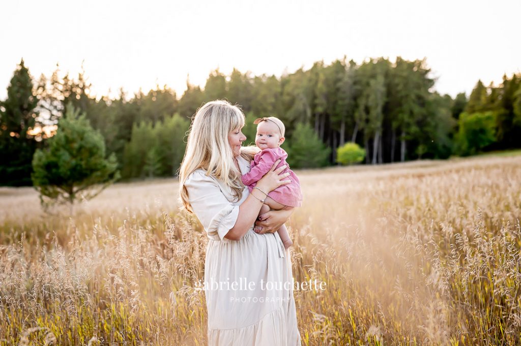A casual mother-daughter portrait taken in tall grass in front of an evergreen forest in the background at birds hill park