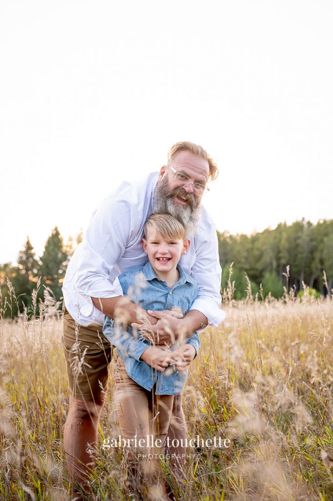 A father hugs and plays with his son in tall grass during a fall photo family session