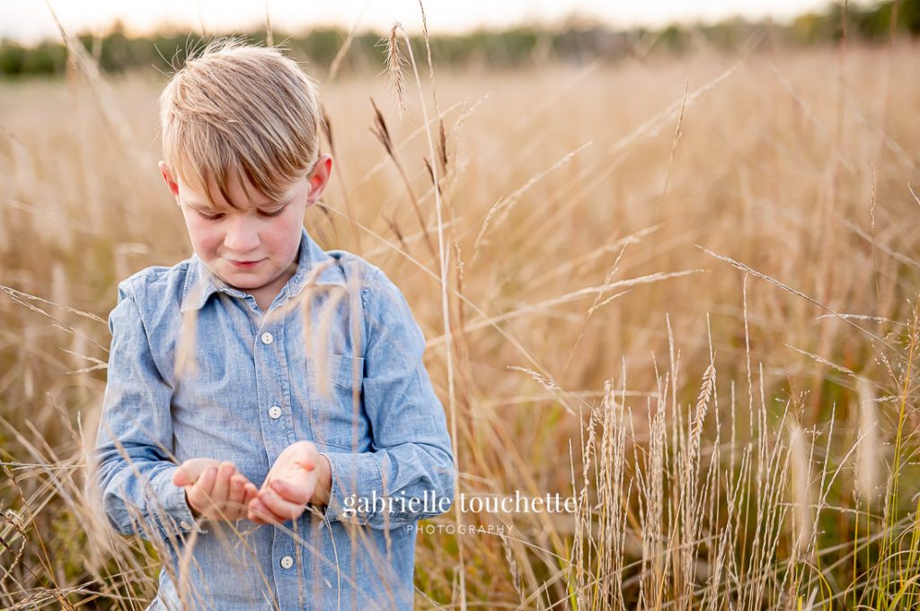 A boy plays with dried grass in a field at birds hill park