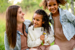 Candid fall family photo in a Winnipeg park of a mother hugging her daughters during a relaxed outdoor photo session capturing genuine emotion and connection.