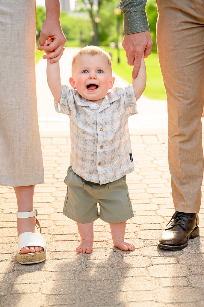 one-year-old hold hands of parents while sunset shines behind him