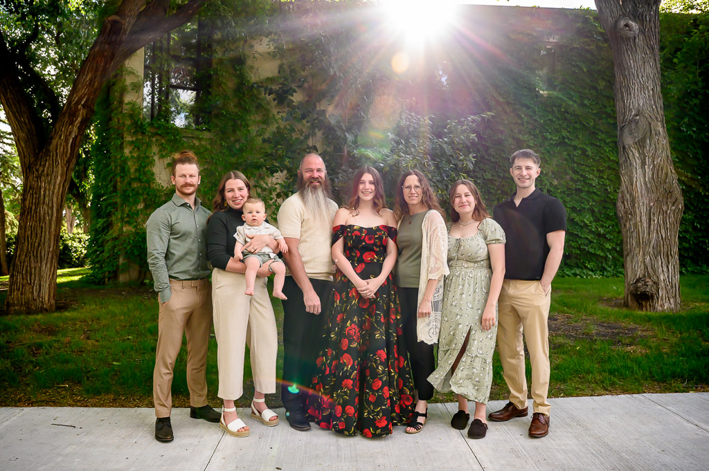 An artistic family photo with a shining sun while the group poses in front of a vine wall in Winnipeg