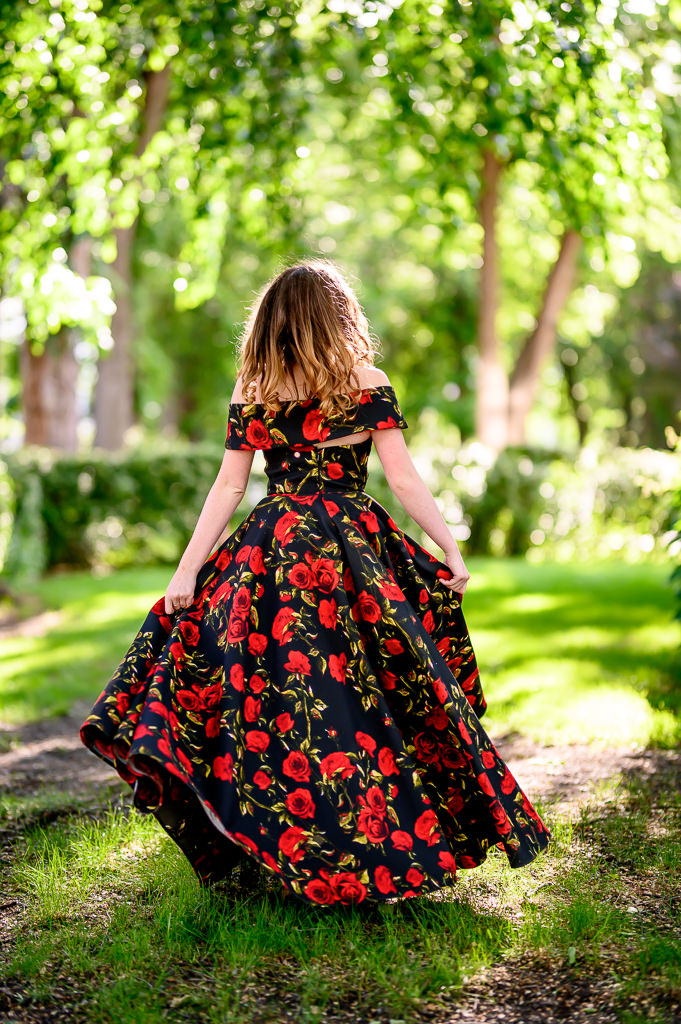 Portrait of a grad in a black and red floral gown walking towards the sunset in a park in Winnipeg