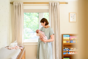 at home newborn photo session with mom holding baby girl in front of the window in the nursery