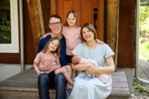 A posed family photo session with a newborn baby and two older sisters taken on the front steps of their house in Winnipeg