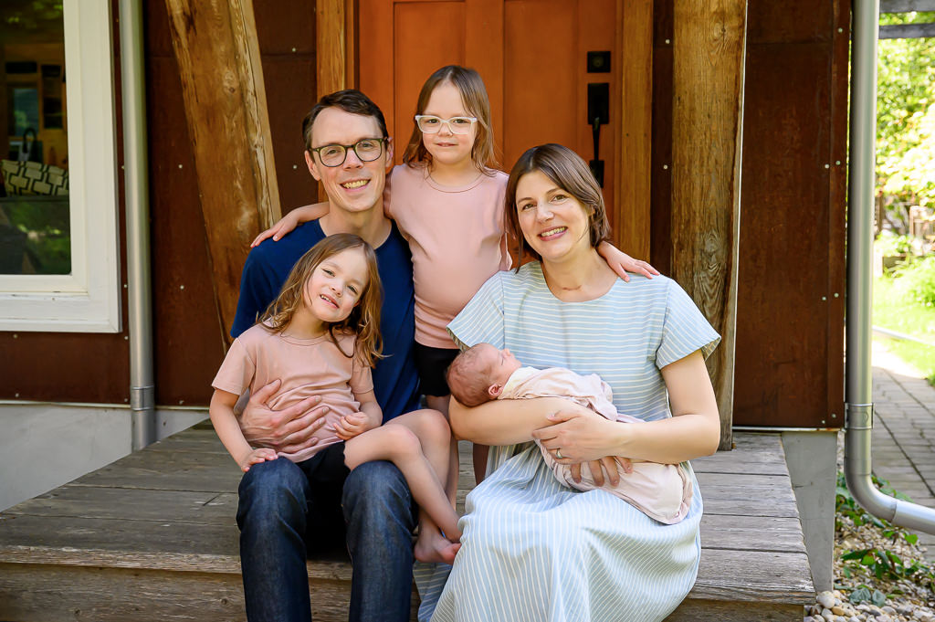 A posed family photo session with a newborn baby and two older sisters taken on the front steps of their house in Winnipeg