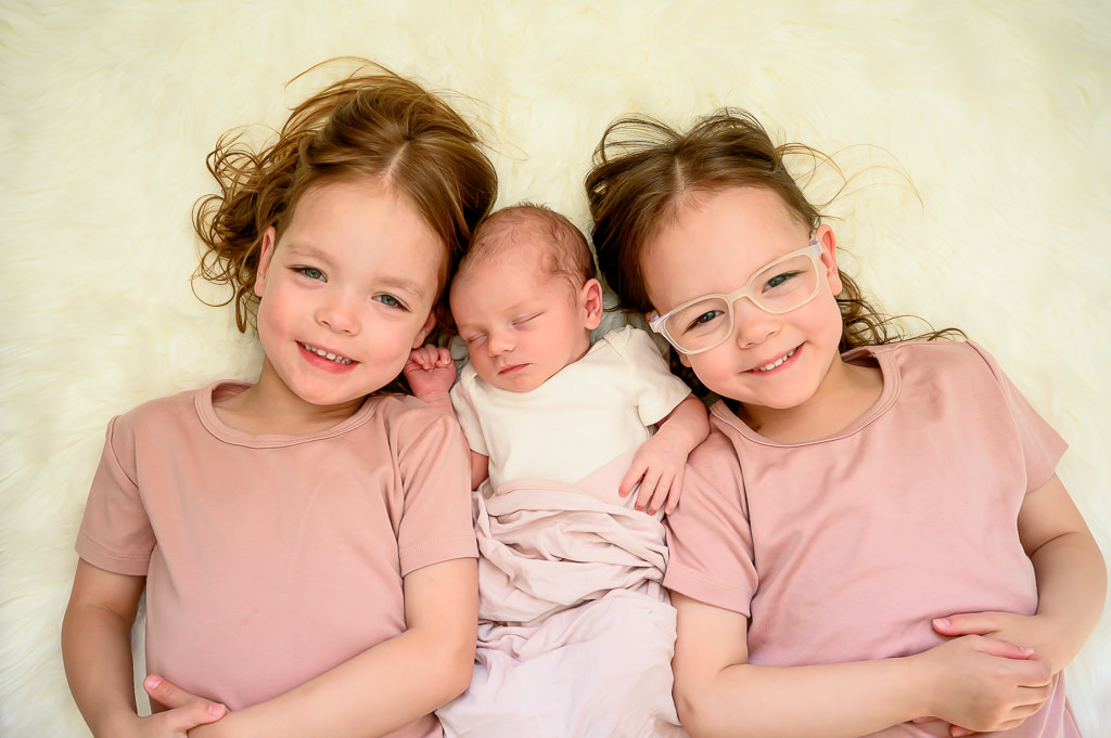 a siblings photo taken at a lifestyle newborn session in Winnipeg with the three sisters smiling together